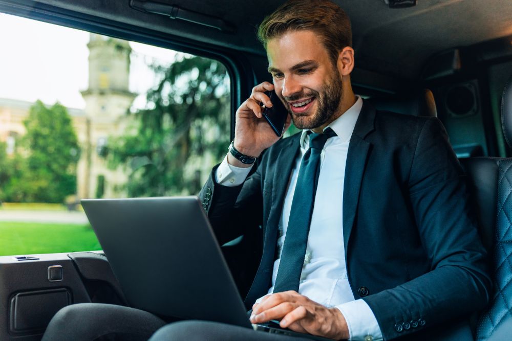 handsome young man in full suit talking on smart phone and working on laptop